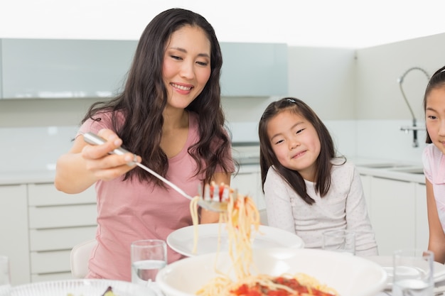 Chicas viendo a mujer feliz servir espaguetis en la cocina