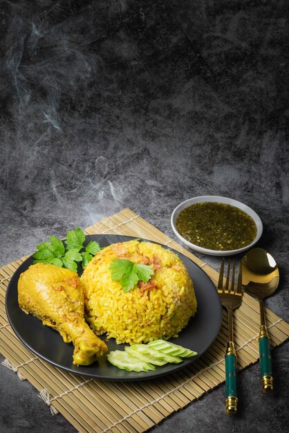 Foto chicken biryani comida tailandesa arroz amarelo marinado com ervas em um prato preto com pernas de frango amarelas