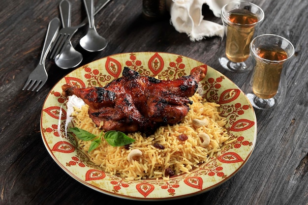 Chicken Dhum Biriyani mit Jeera-Reis und Gewürzen, serviert mit Tee in Keramikplatte auf schwarzem rustikalem Holzhintergrund