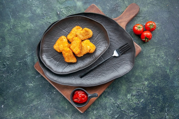 Chicken Nuggets auf schwarzem Teller und Gabel auf Holzbrett Tomatenketchup auf dunkler Oberfläche