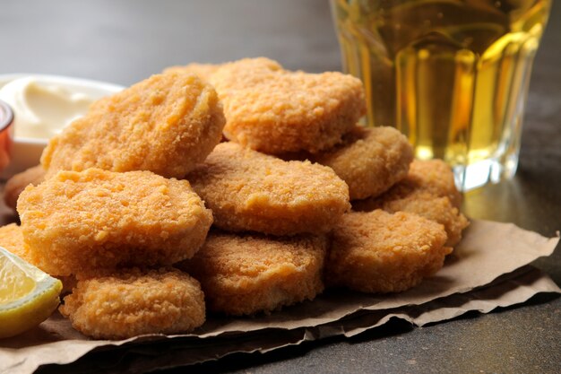 Chicken Nuggets mit weißer und roter Soße und Bier und Zitrone auf braunem Hintergrund. Fast-Food-Nahaufnahme