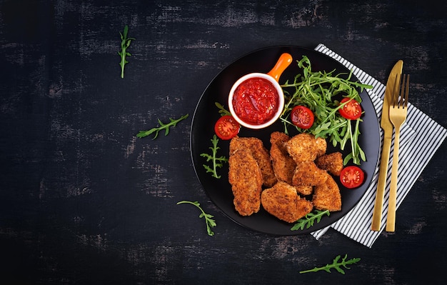 Chicken Nuggets und Sauce in schwarzer Platte auf dunklem Hintergrund. Ansicht von oben, oben