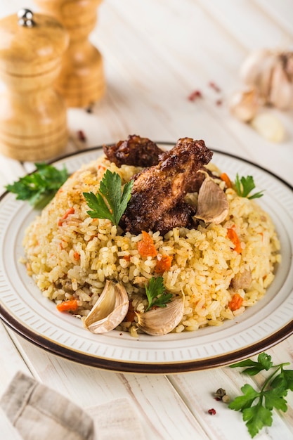 Foto chicken pilaw in einem hellen teller mit gebackenem knoblauch und frischen kräutern auf weißem holzhintergrund. ein traditionelles orientalisches gericht. vertikale ausrichtung.