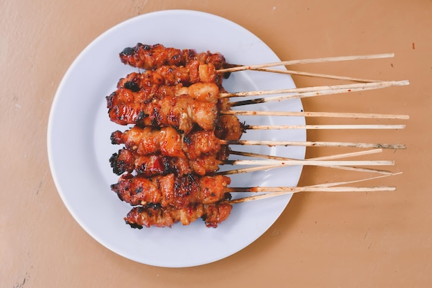 Chicken Satay oder Chicken Skin Satay mit roten Gewürzen auf weißem Teller isoliert auf Holztischen