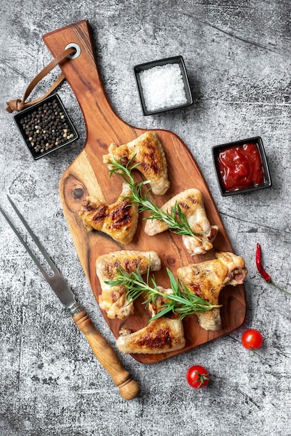 Chicken Wings auf einem Holzbrett mit Gewürzen und Kräutern.