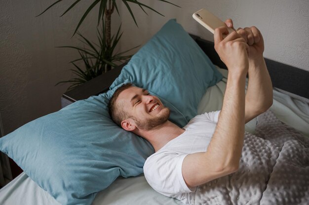 Un chico acostado en la cama tomando selfies