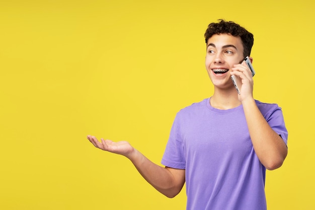 Un chico adolescente guapo y sonriente sosteniendo un teléfono móvil contestando una llamada explicando algo