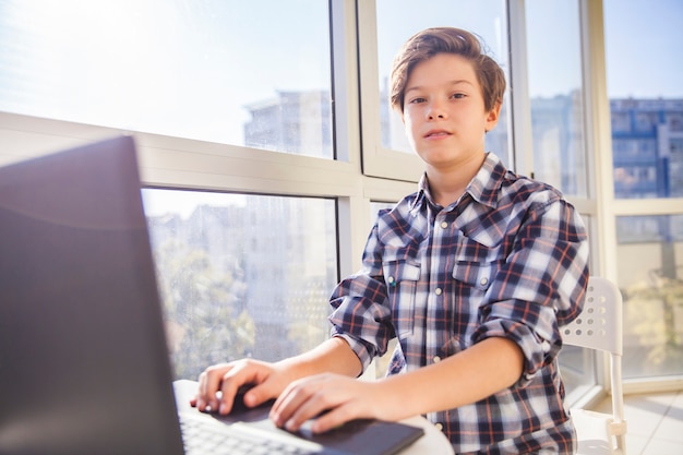 Foto chico adolescente usando laptop por ventana