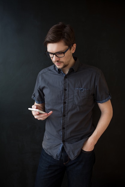 Chico adulto joven en una camisa gris utiliza un teléfono inteligente. Retrato de negocios en negro con textura