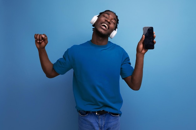 Chico africano en una camiseta escucha música con auriculares y teléfono inteligente