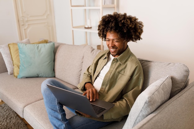 Chico africano escribiendo en una computadora usando una computadora portátil para trabajar en interiores