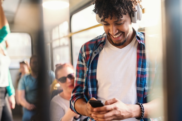 Chico africano joven escuchando la música y usando el teléfono inteligente mientras viajaba en transporte público.