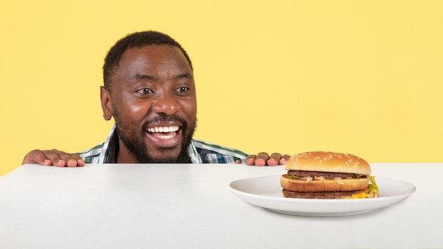 Chico africano mirando Burger en mesa sobre fondo amarillo