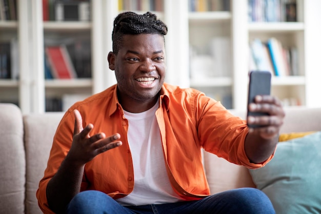 Chico africano sonriente tiene videollamada por teléfono en casa