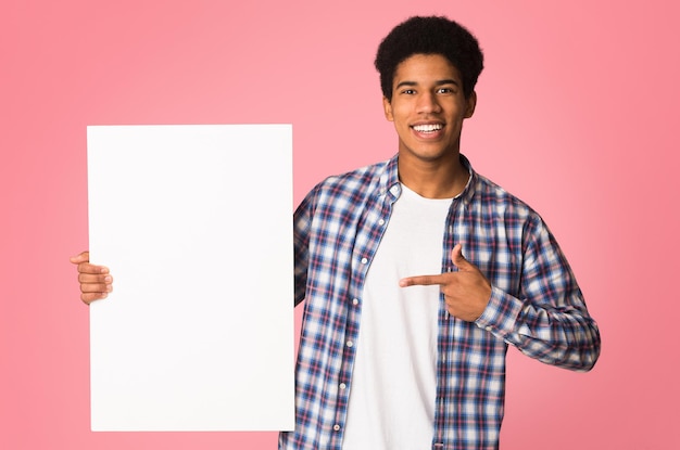 Chico afroamericano apuntando al fondo rosa de la pancarta en blanco