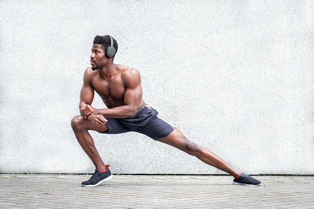 Chico afroamericano de deportes haciendo ejercicio al aire libre contra la pared hombre atlético haciendo calentamiento