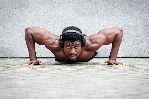 Chico afroamericano entrenando al aire libre contra el fondo de la pared hombre con cuerpo atlético haciendo calentamiento