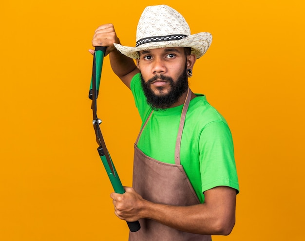 Chico afroamericano joven jardinero confiado con sombrero de jardinería sosteniendo tijeras