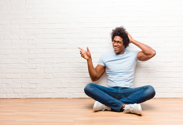 un chico afroamericano sentado dándose cuenta de una gran idea apuntando a lateral