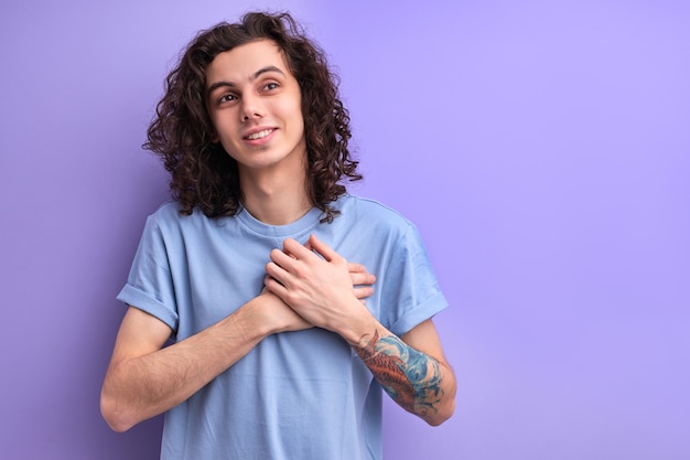 Chico agradable con el pelo rizado mantener las manos en el pecho masculino está agradecido por todo decir gracias sonriendo ...