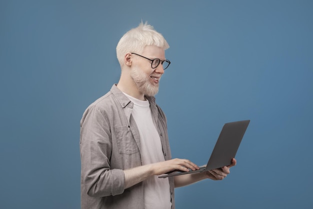 Chico albino feliz que trabaja en línea en una computadora portátil mientras navega por internet azul