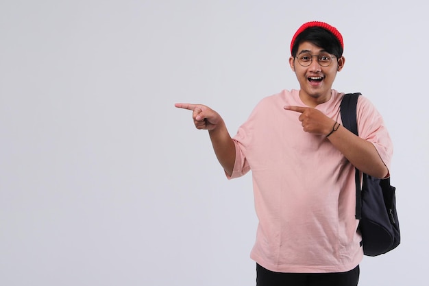 Chico alegre joven casual con mochila apuntando sus dedos al espacio en blanco