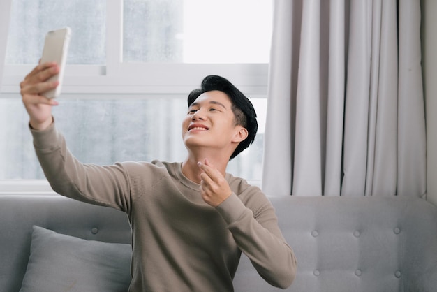 Chico alegre joven haciendo selfie en teléfono inteligente y sentado en el sofá