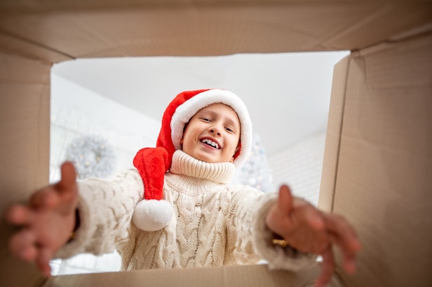 Chico alegre niño lindo abriendo un regalo de Navidad. Niño divirtiéndose cerca del árbol de Navidad en el interior. Vista desde el interior de la caja ¡Feliz Navidad y Felices Fiestas!