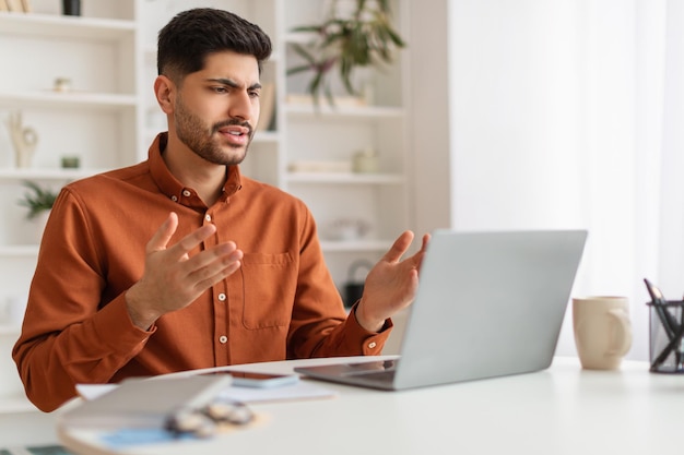 Chico árabe confundido usando una computadora portátil mirando la pantalla