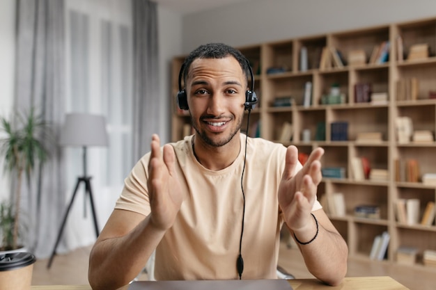 Chico árabe independiente positivo en auriculares con videollamada en línea hablando con un socio comercial y