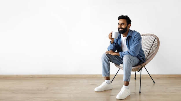 Chico árabe posando con una taza tomando café sobre una pared blanca