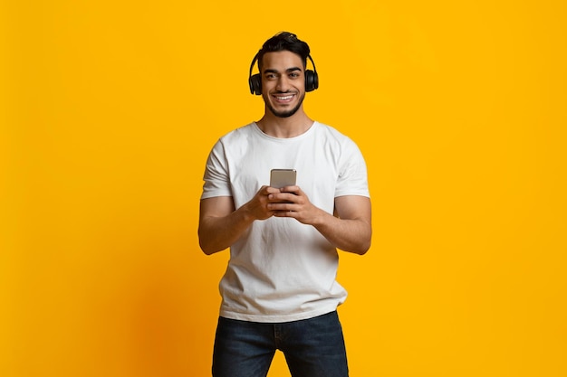 Chico árabe positivo usando auriculares inalámbricos y espacio de copia de teléfono inteligente