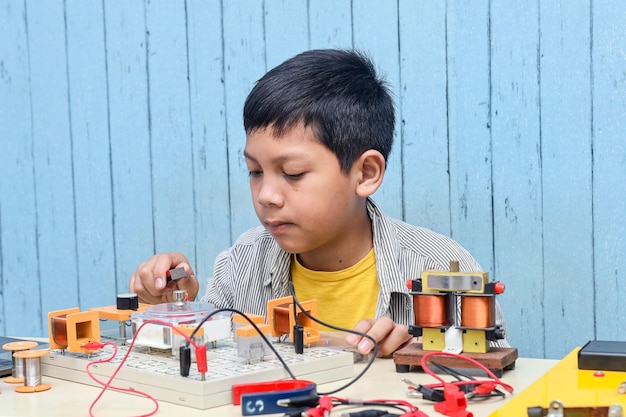 Chico asiático de aspecto inteligente que trabaja con circuitos, cables, computadora, motor en su proyecto. ciencia, tecnologia