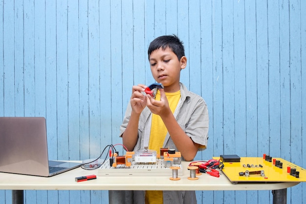 Chico asiático de aspecto inteligente que trabaja con circuitos, cables, computadora, motor en su proyecto. ciencia, tecnologia