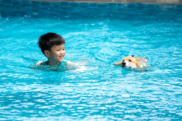 Chico asiático y cachorro de perro Corgi juegan en la piscina