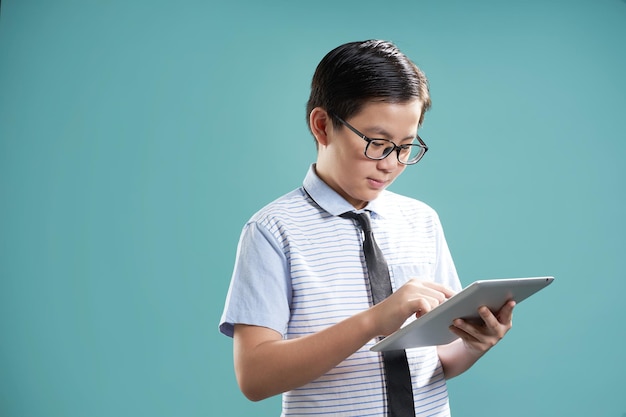 Chico asiático inteligente usando tableta digital para aprender aislado sobre fondo verde menta