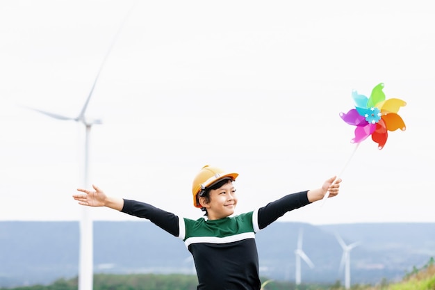 Chico asiático joven progresivo jugando con juguete de molinillo de viento en la granja de turbinas eólicas