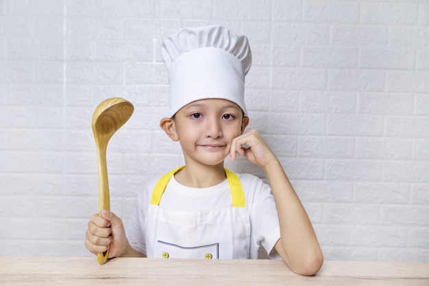 Foto chico asiático lindo con delantal y gorro de cocinero en la pared de ladrillo blanco.