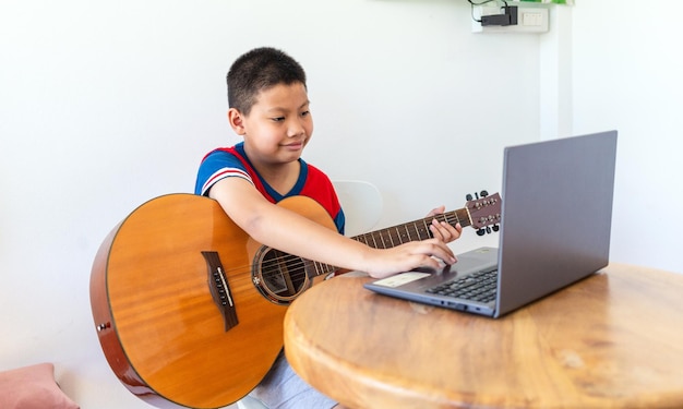 Un chico asiático lindo practica tocar la guitarra en línea.