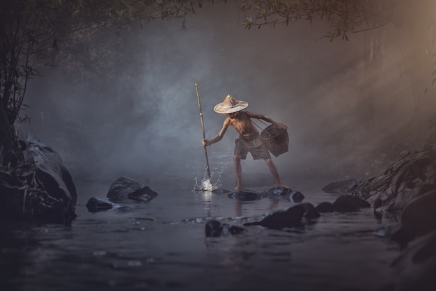 Chico asiático pescando en el arroyo, campo de Tailandia