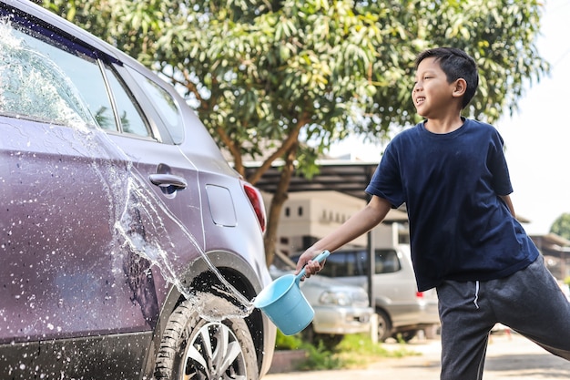 Chico asiático salpicar agua con un cazo para mojar el coche