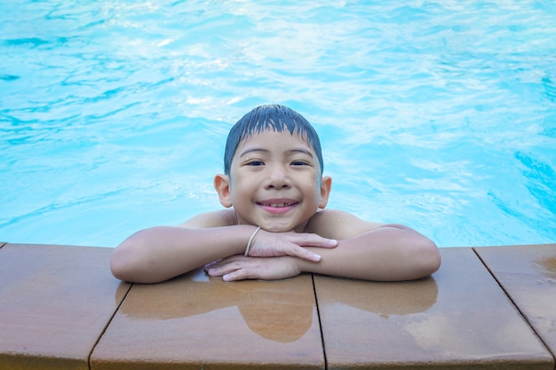 Chico asiático sonriendo en el borde de la piscina azul