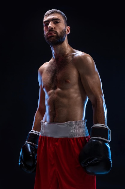 Chico atlético guapo en un pantalón rojo sobre un fondo negro el boxeador está recuperando el aliento después de p ...