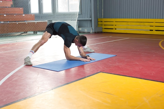 Chico atlético en ropa deportiva y rastreador de fitness haciendo ejercicios en el gimnasio.