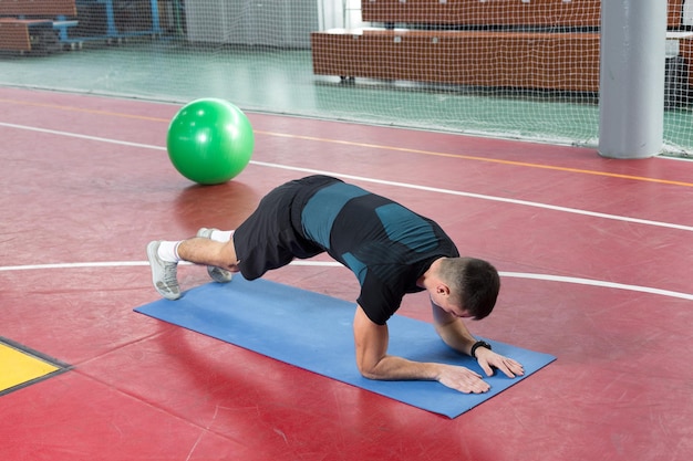 Chico atlético en ropa deportiva y rastreador de fitness haciendo ejercicios en el gimnasio