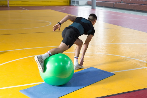 Chico atlético en ropa deportiva y rastreador de fitness haciendo ejercicios en el gimnasio.