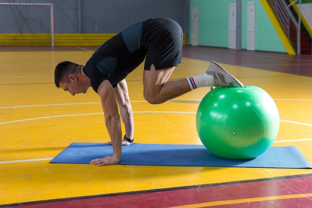 Chico atlético en ropa deportiva y rastreador de fitness haciendo ejercicios en el gimnasio.