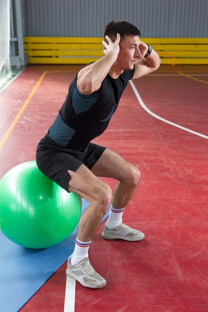 Chico atlético en ropa deportiva y rastreador de fitness haciendo ejercicios en el gimnasio.