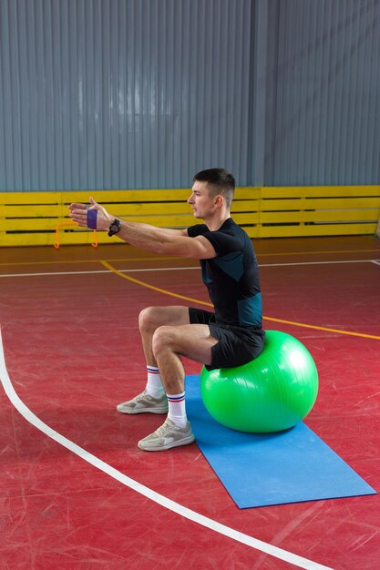 Chico atlético en ropa deportiva y rastreador de fitness haciendo ejercicios en el gimnasio.