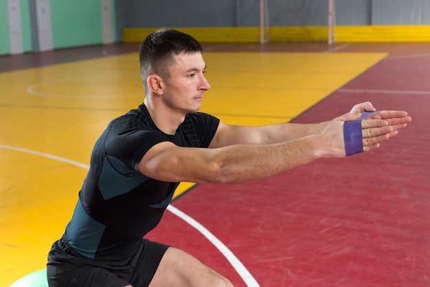 Chico atlético en ropa deportiva y rastreador de fitness haciendo ejercicios en el gimnasio.